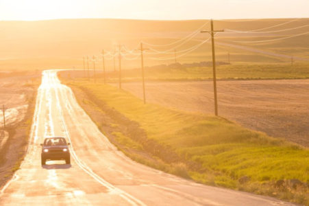 lone car on Montana road looking golden at early sunrise